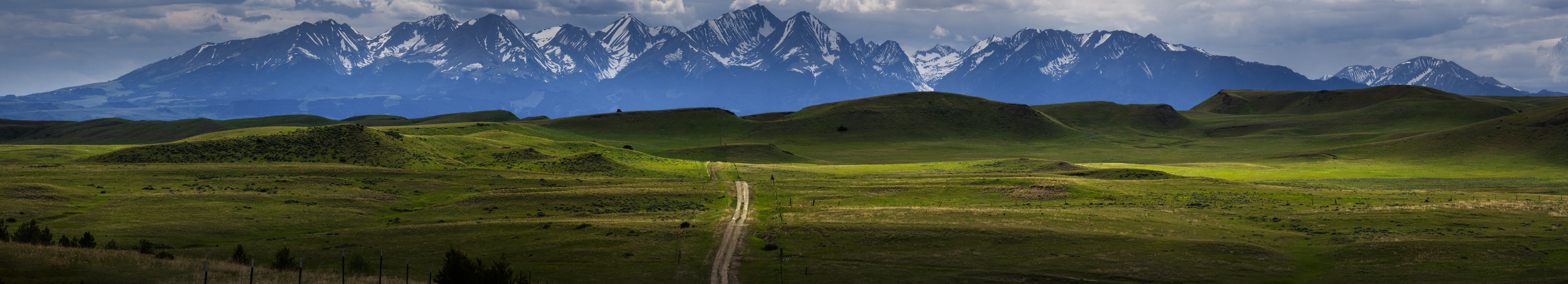 A dirt road winding through green hills toward the Crazy Mountains